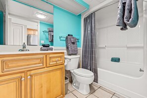 A bathroom with a wooden vanity, a toilet, a bathtub, and a shower curtain. - Oceanfront Retreat with Resort Pools (Myrtle Beach)