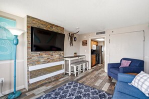 Una sala de estar con televisión, chimenea, sofá, comedor y cocina al fondo.