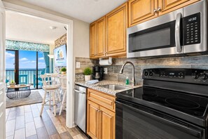 A modern kitchen with stainless steel appliances, wooden cabinets, and a view to a balcony. - Oceanfront Retreat with Resort Pools (Myrtle Beach)