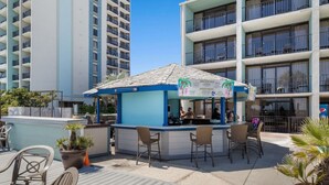A rooftop bar with outdoor seating, a blue and white color scheme, and a menu board advertising cocktails.