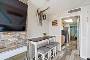 A kitchen with a stone backsplash, a wooden bar with two stools, a mounted deer head, and a kitchen island. - Oceanfront Retreat with Resort Pools (Myrtle Beach)
