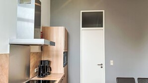 Une cuisine compacte équipée d’une cuisinière intégrée, d’une machine à café et d’un four à micro-ondes. On y trouve une porte blanche et un petit coin repas avec une table et des chaises.