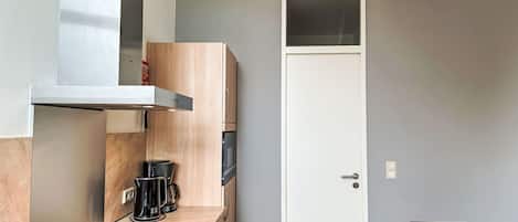 Una cocina compacta con estufa integrada, cafetera y microondas. Cuenta con una puerta blanca y un pequeño comedor con mesa y sillas.
