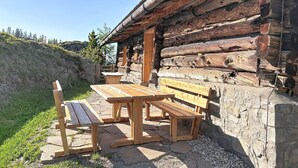 Tunnelmallinen, maalaishenkinen puumökki, jossa on kivinen pohja, puiset penkit ja piknikpöytä.