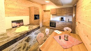 A cozy wooden cabin interior with a dining table, chairs, a kitchen area, and a fireplace. - Sennerin by Interhome (Forstau)
