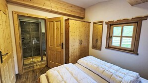 A bedroom with a wooden wardrobe, a glass shower enclosure, and a window with a view. - Sennerin by Interhome (Forstau)