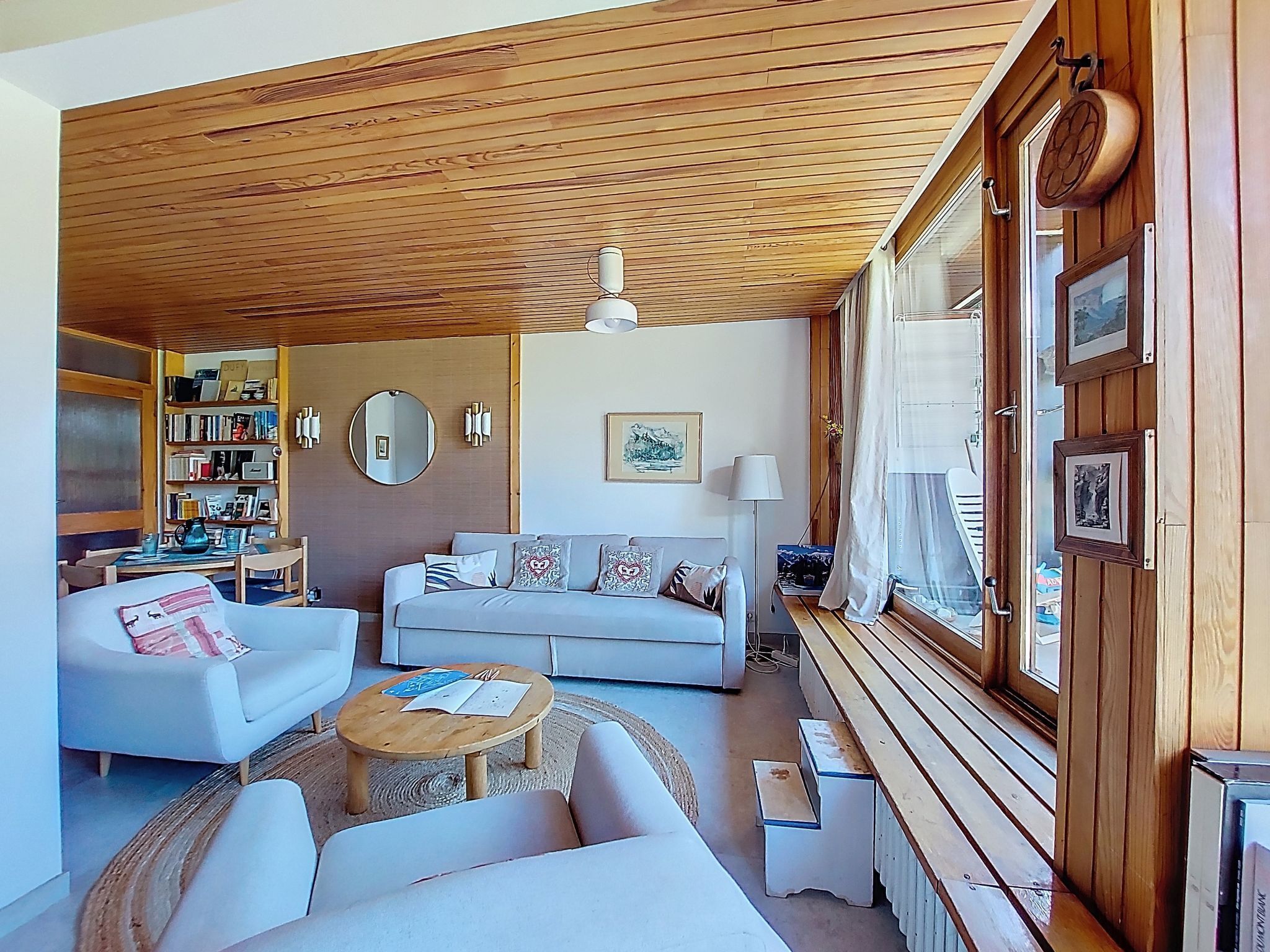 A cozy living room with a wooden ceiling, a sofa, a coffee table, and a bookshelf.