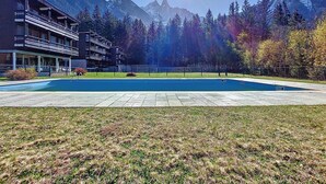 A swimming pool with a mountain backdrop, a multi-story building, and a grassy area. - Résidence Les Tines by Interhome (Chamonix - Les Praz)