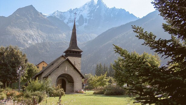 A small stone church with a pointed steeple, surrounded by a well-maintained garden with red flowers and a stone pathway leading to it. - Résidence Les Tines by Interhome (Chamonix - Les Praz)