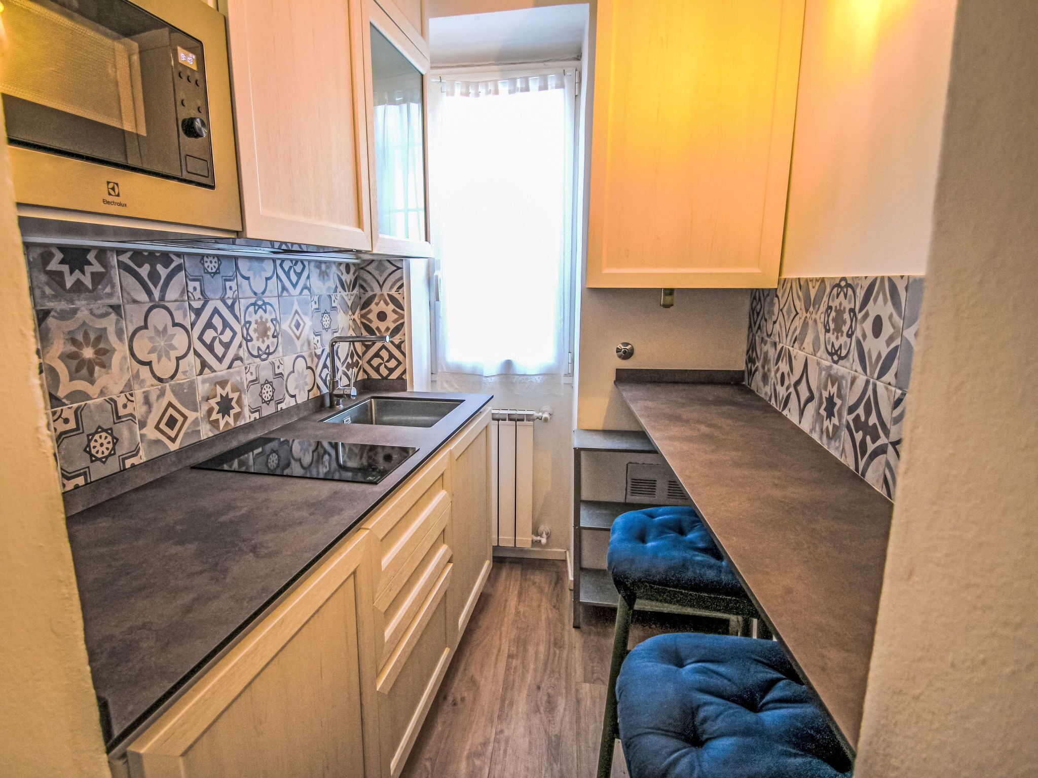 A compact kitchen with a built-in stove, a sink, and a window with curtains.
