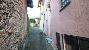 Un estrecho callejón entre edificios, con paredes de piedra a un lado y un edificio rosa al otro.
