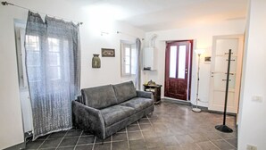 Una sala de estar con un sofá gris, una puerta roja y un suelo de baldosas.