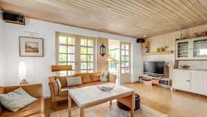 Ein geräumiges Wohnzimmer mit Holzboden, einer Sofagarnitur, einem Fernseher und einer Küchenzeile mit Schränken und einem Fernseher.