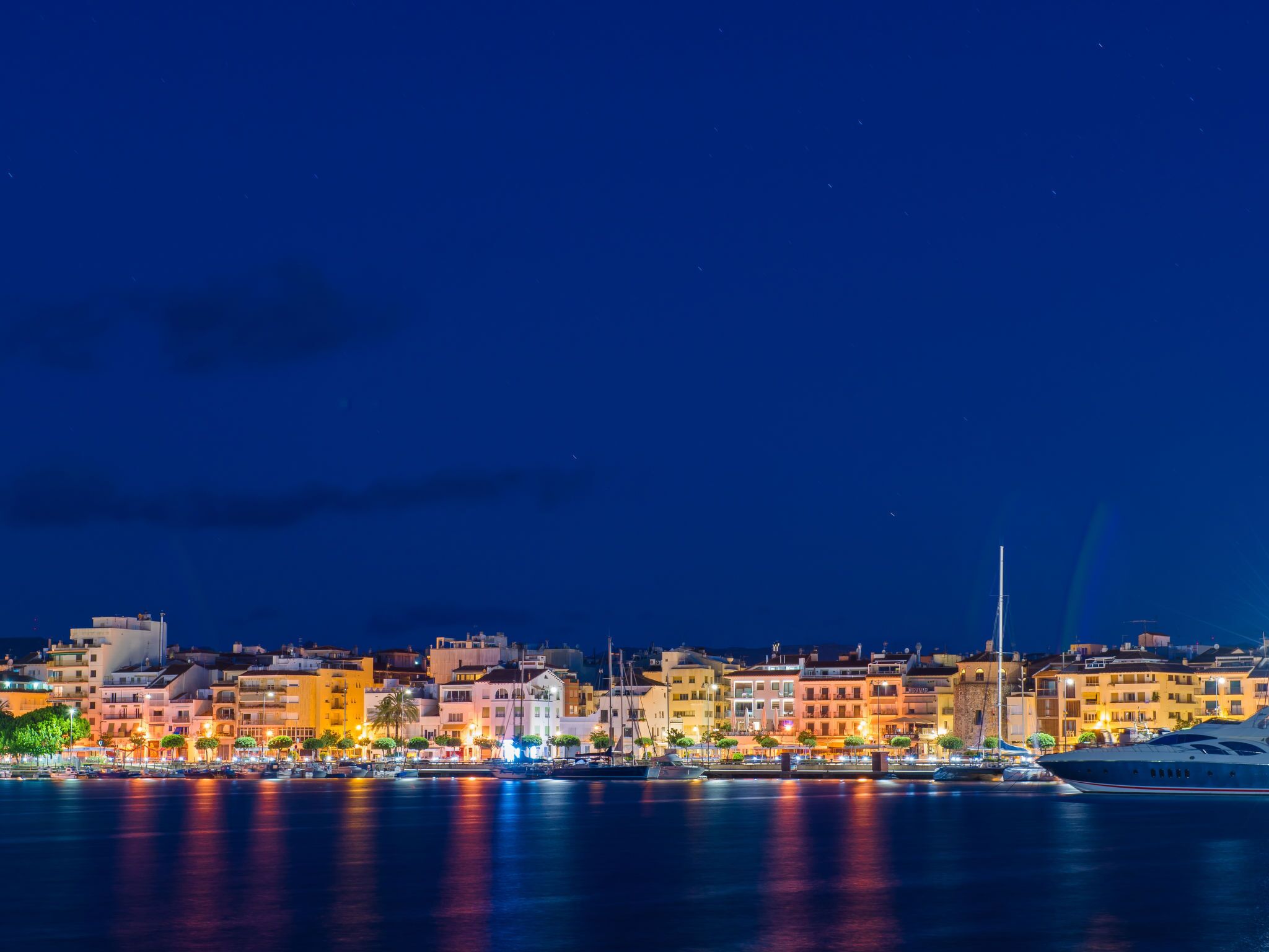 A waterfront cityscape at night with illuminated buildings and boats.