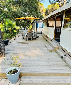 Une terrasse en bois avec des meubles d’extérieur, un espace salon couvert et une grande plante en pot.