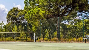 Uma quadra de tênis com rede, rodeada por árvores e uma cerca.