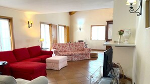 Ein Wohnzimmer mit einem roten Sofa, einem blumengemusterten Sofa und einem weißen Sofa. Ein Fernseher, ein kleiner Tisch und ein Wagen mit Gegenständen sind ebenfalls vorhanden.