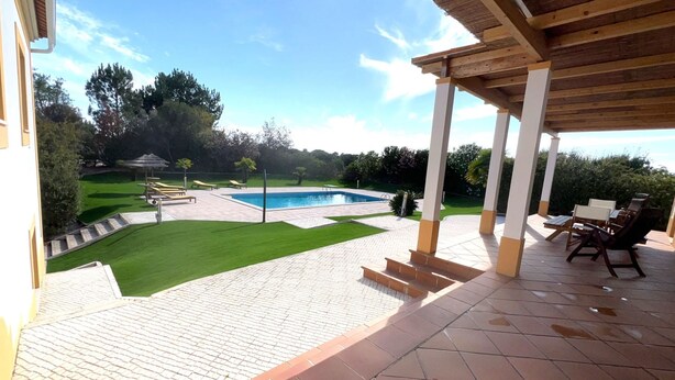 Ein überdachter Außenbereich mit Pool, Terrassenmöbeln und einem gepflegten Rasen.