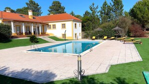 Ein Haus mit Swimmingpool, einer Terrasse mit Liegestühlen und einem gepflegten Rasen.