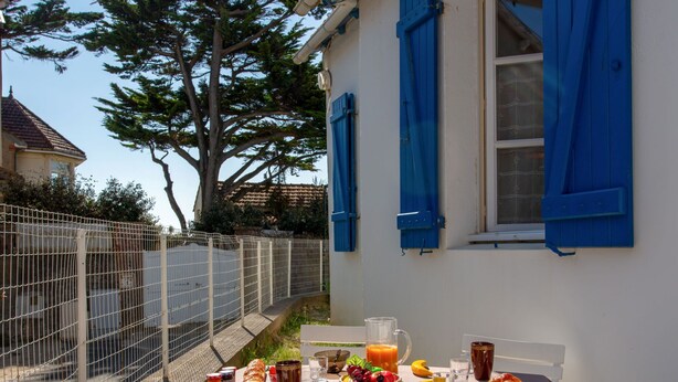 Una mesa al aire libre con mantel, comida, bebidas y una cesta de fruta.