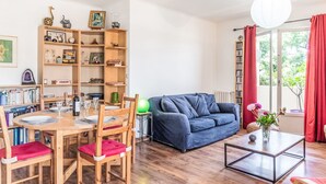 A cozy living room with a dining area, wooden furniture, a blue sofa, and a bookshelf filled with books and decorative items.