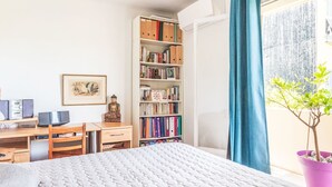 A bedroom with a bed, a desk with a computer, a bookshelf, and a window with curtains.