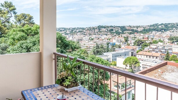A balcony with a view of a cityscape, a potted plant, and a tiled table.