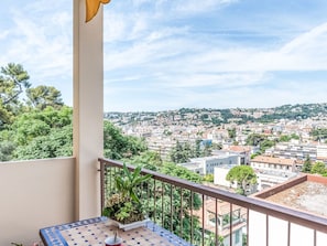 Un balcón con vista a un paisaje urbano, una planta en maceta y una mesa de baldosas.