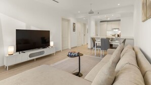 En moderne stue med et fladskærms-tv, en sofa, et sofabord og et spiseområde med bord og stole.