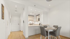 Et moderne køkken med hvide skabe, en central ø og et spiseområde med bord og stole.