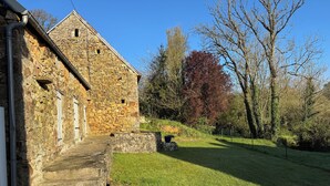 A stone building with a staircase leading up to a door, surrounded by a grassy area and trees.
