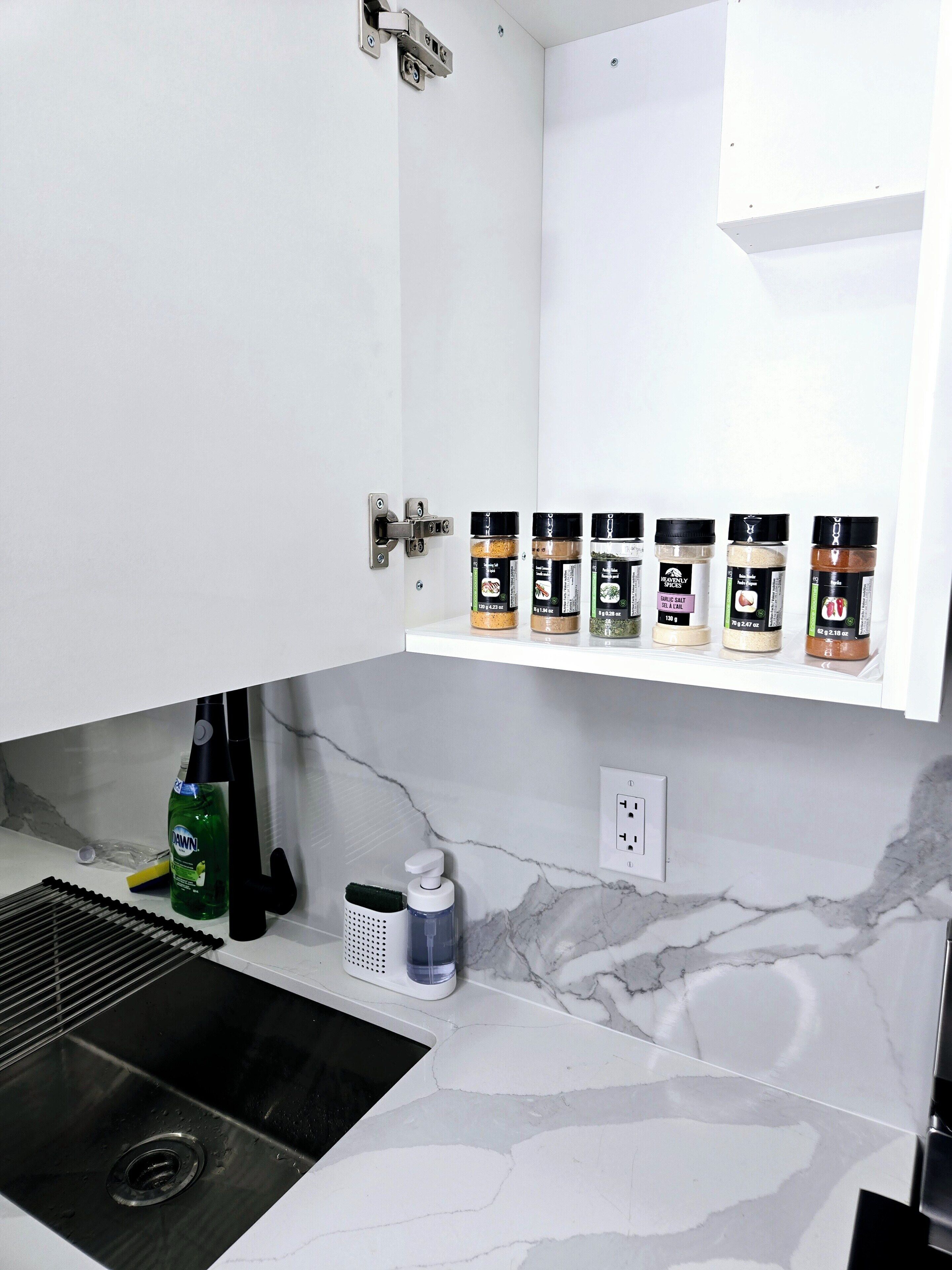 Eine Küche mit weißer Arbeitsplatte, Spüle und einer Marmor-Spritzschutzwand. Über der Spüle befinden sich Gewürzregale.