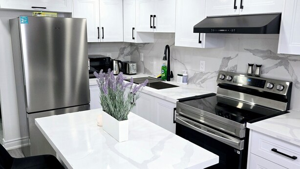 A modern kitchen with white cabinets, stainless steel appliances, and a marble backsplash.