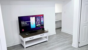 A modern living room with a flat-screen TV on a white TV stand, grey flooring, and a grey sofa.