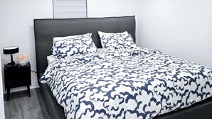 A modern bedroom with a large bed, a bedside table with a lamp, and a window with blinds.