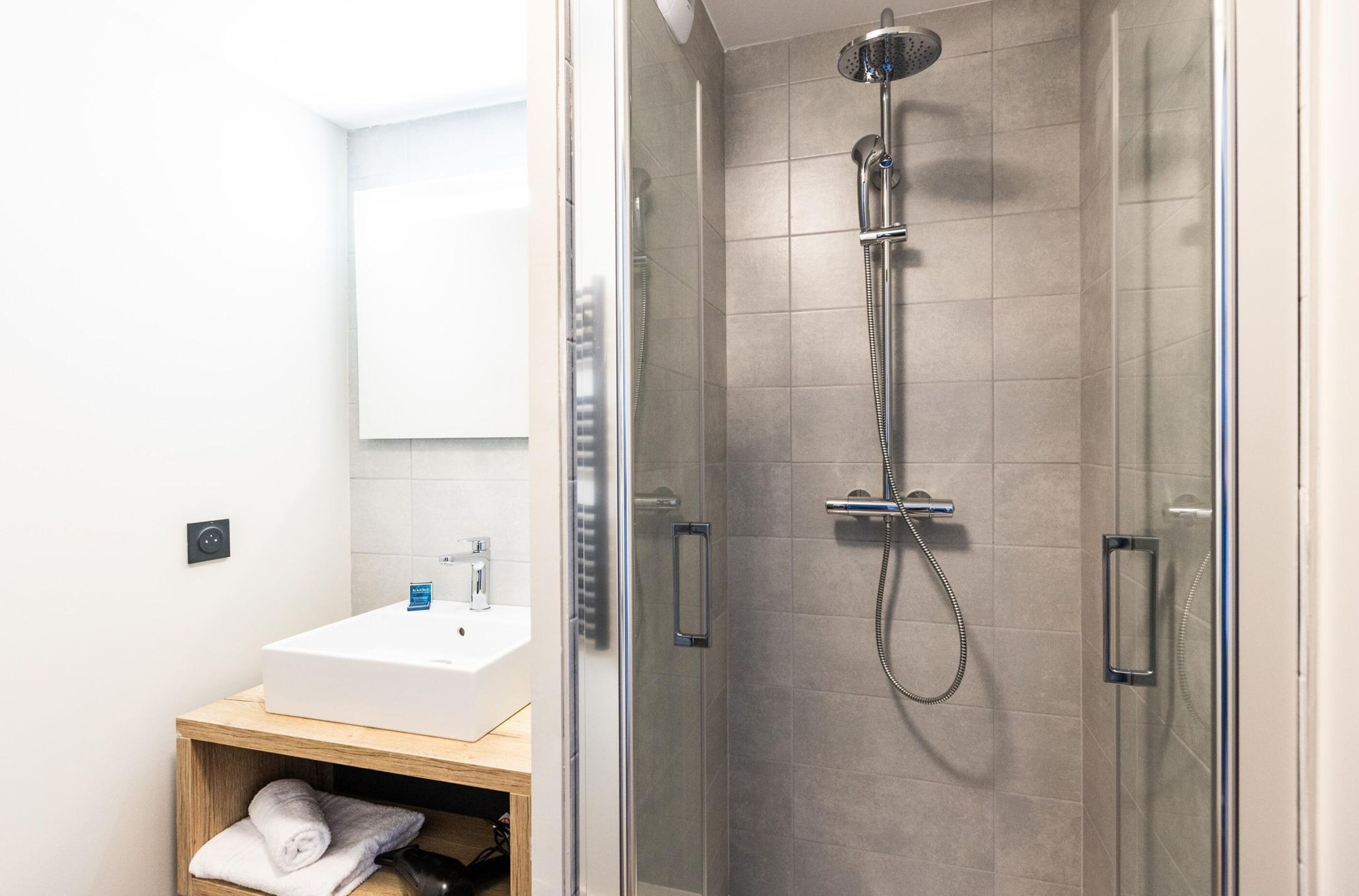 A modern bathroom with a glass-enclosed shower, a white sink, and a wooden vanity.