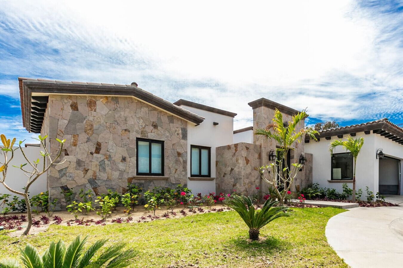A modern house with stone walls, a well-maintained garden, and a clear sky.