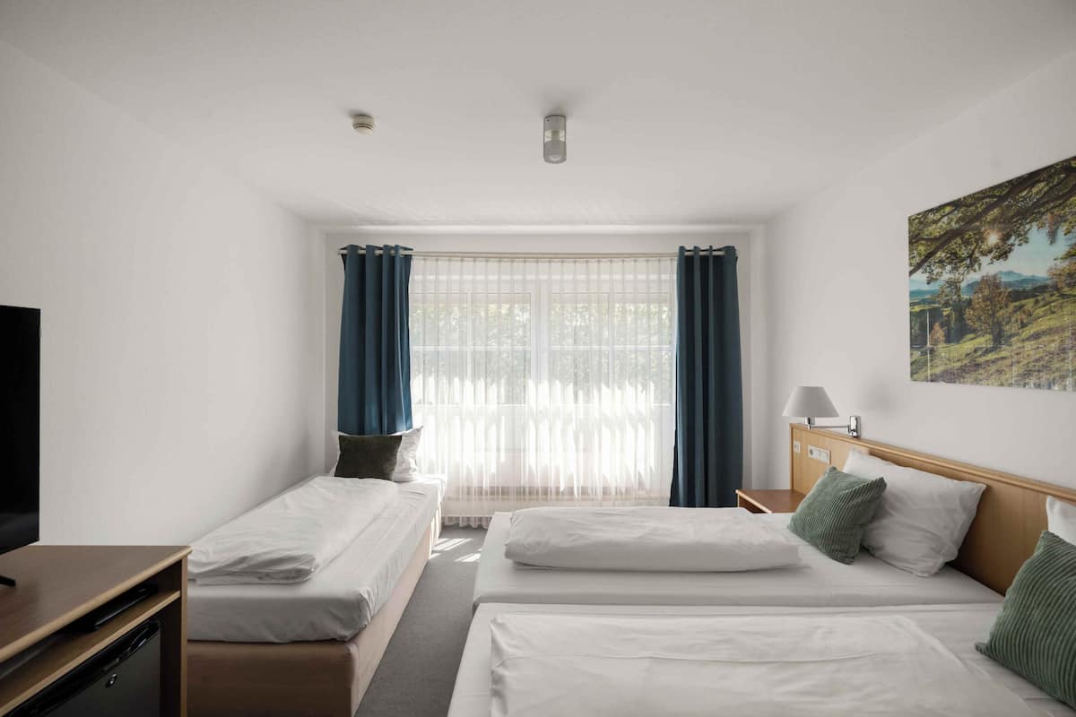 A hotel room with two beds, a desk, a TV, and a window with curtains.