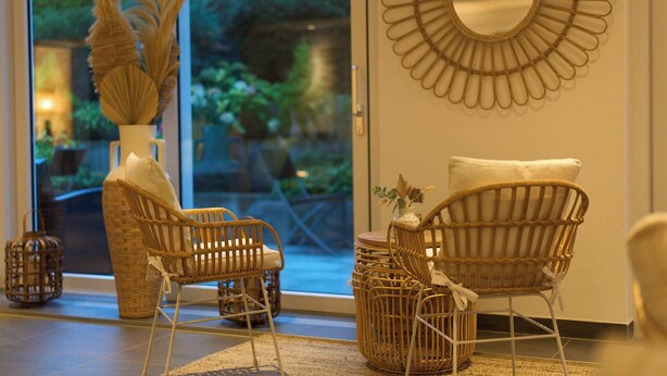 A room with wicker furniture, a large mirror, and a view of greenery outside.