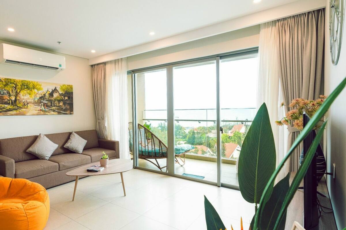 Un salon moderne comprenant un canapé, une table basse, un fauteuil poire, une chaise et une grande fenêtre donnant sur un beau paysage.