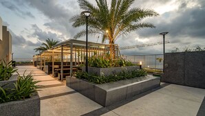Um terraço ao ar livre com área de estar coberta, palmeiras e vista para o mar.