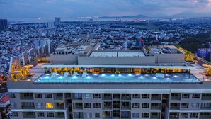 Um hotel moderno e alto, com vários andares, piscina no terraço e vista panorâmica da cidade.