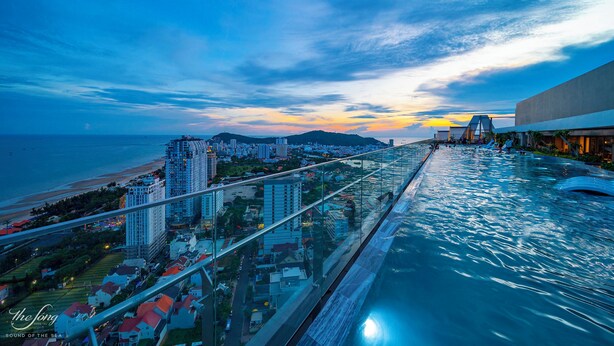 Um edifício alto com piscina no terraço com vista para a praia e o horizonte da cidade.