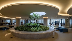 Um lobby moderno com um vaso circular central, áreas de estar e um design de teto curvo.