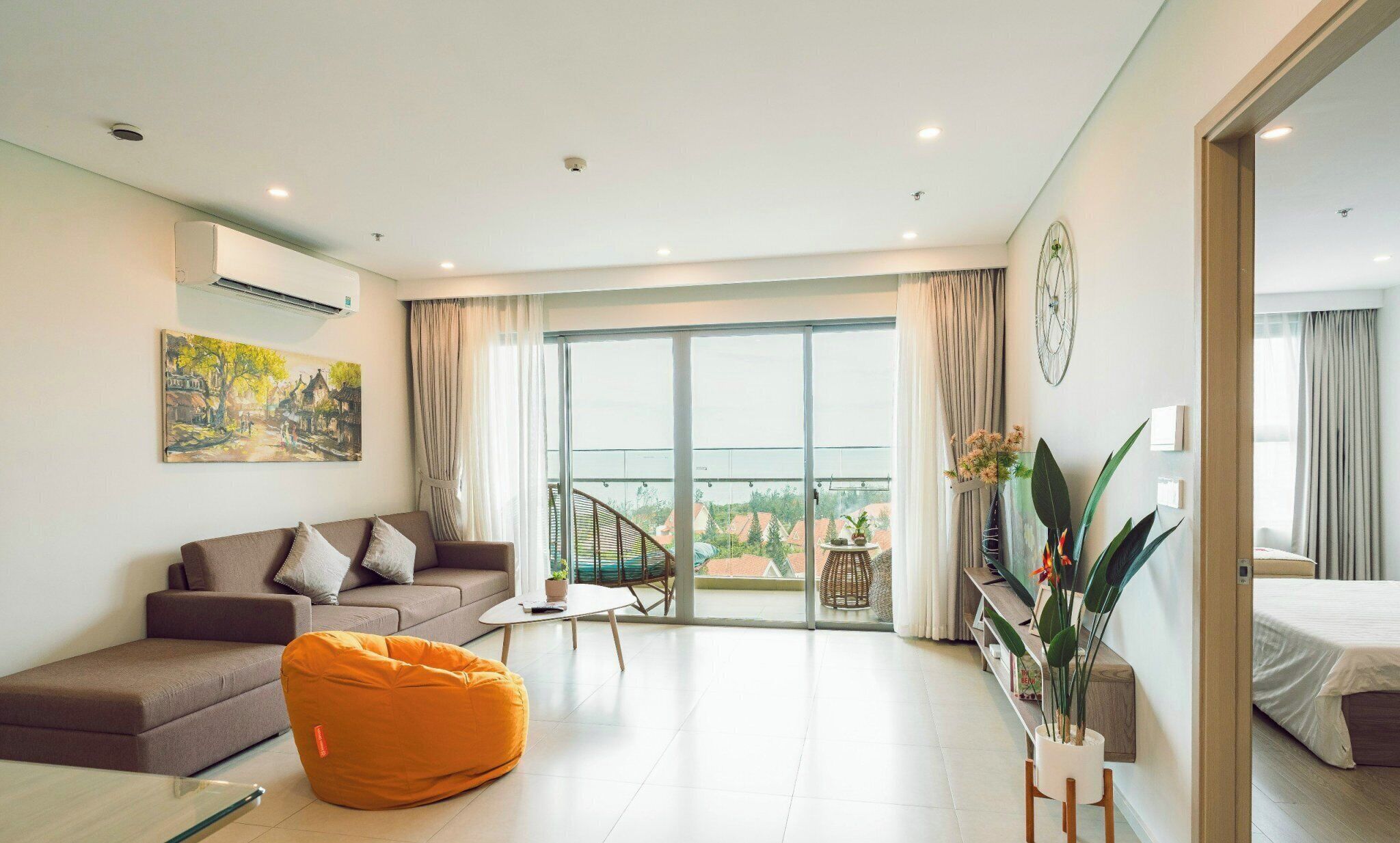 A modern living room with a sofa, a bean bag, a coffee table, and a balcony with a view of houses.