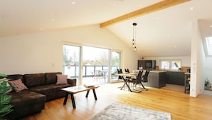 A spacious living area with a wooden floor, a sofa, a coffee table, and a dining table with chairs. There is a kitchen area with a sink and cabinets, and a large window providing natural light. - Penthouse suite with romantic whirlpool in privacy. Ideal for couples (Rosenheim)