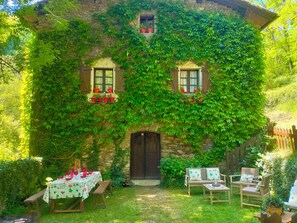 Una casa in pietra con muri ricoperti d'edera, una porta in legno e un patio con tavolo e sedie.