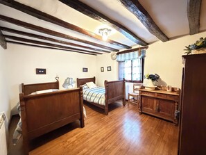 Una camera da letto con due letti di legno, una cassettiera in legno, una finestra con tende e un soffitto con travi a vista.