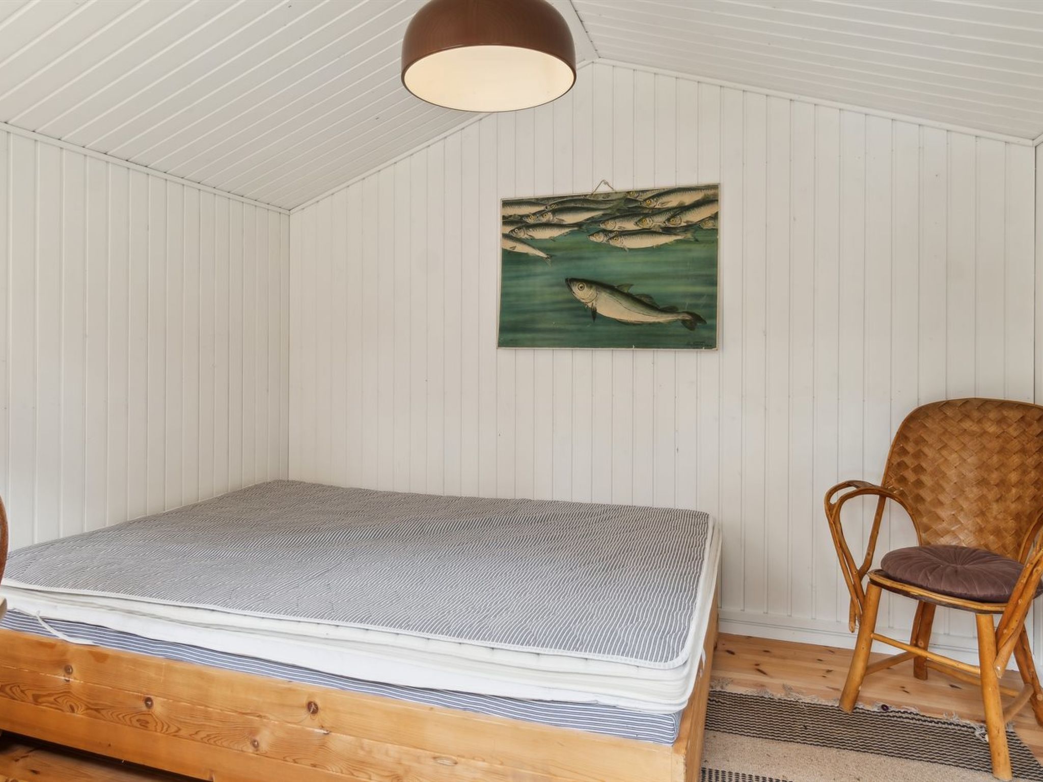 Une pièce avec un lit, une chaise et un tableau représentant des poissons accroché au mur.
