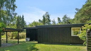 A modern, single-story building with a flat roof, a small window, and a covered outdoor area with a grill.